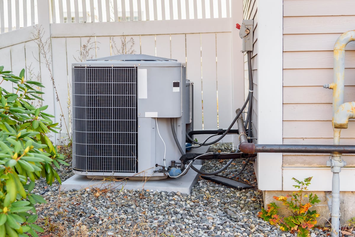 Exterior heat pump unit beside a wooden fence in a backyard