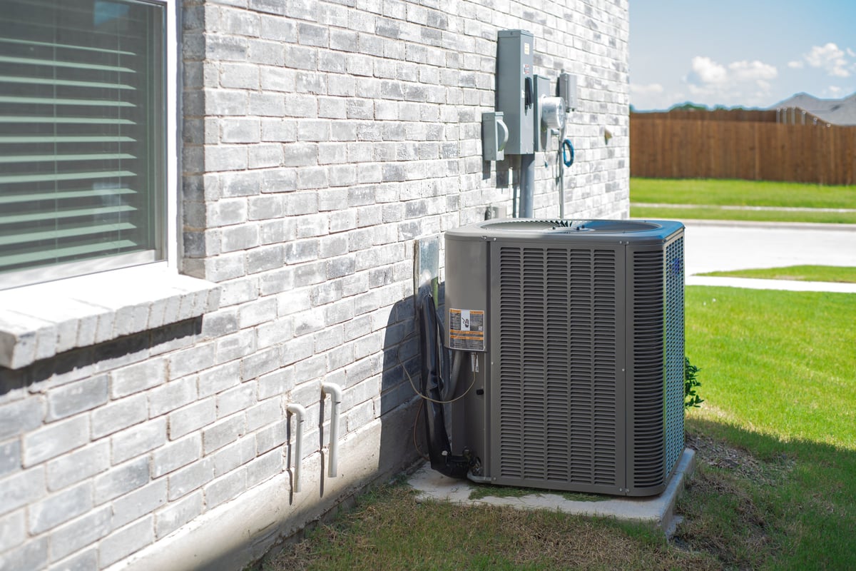 Central air conditioning condenser unit mounted beside a brick home
