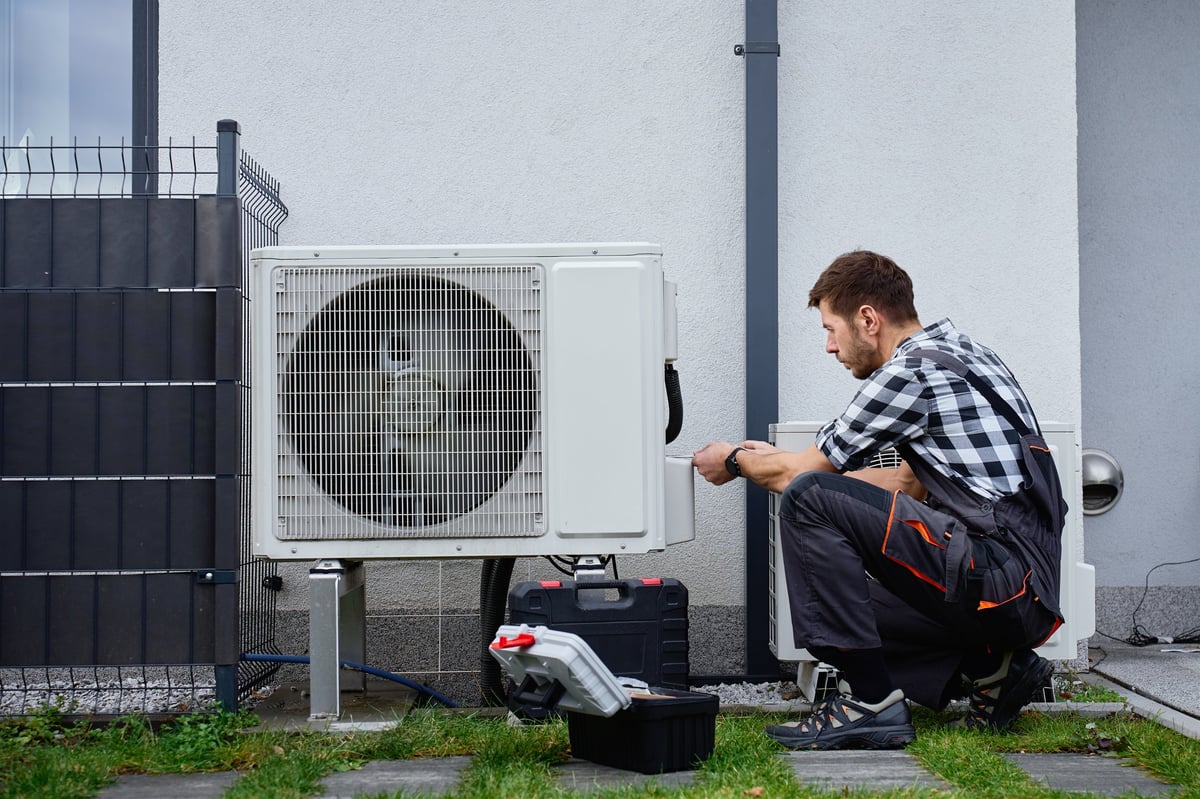HVAC technician servicing an outdoor heat pump unit at a home